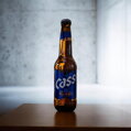 Estetický záber fľaše obľúbeného kórejského piva Cass fresh (330 ml) stojacej na drevenom stole v presvetlenom interiéri. Charakteristická modrá etiketa s nápisom Cold Brewed a obsahom alkoholu 4,5 % vol. Jasné nasvietenie fľaše zvýrazňuje zlatistú farbu 