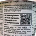 Detail bočnej strany obalu s veľkým čierno-bielym QR kódom. Podľa sprievodného textu v štyroch európskych jazykoch (nemčina, francúzština, taliančina, poľština) kód odkazuje na podrobný návod na prípravu. Nad kódom je viacjazyčný pokyn upozorňujúci na nut
